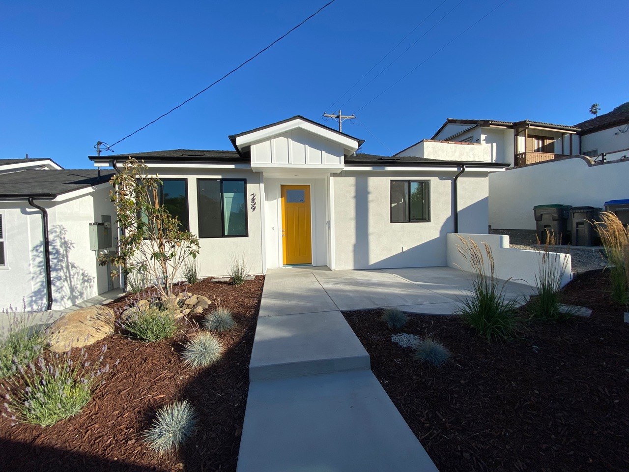 Completed modern single-story home with fresh stucco, yellow entry door, and drought-tolerant landscaping
